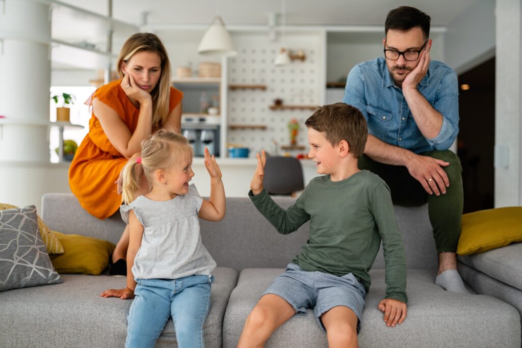 Tired parents sitting on couch feels annoyed exhausted while happy children playing together